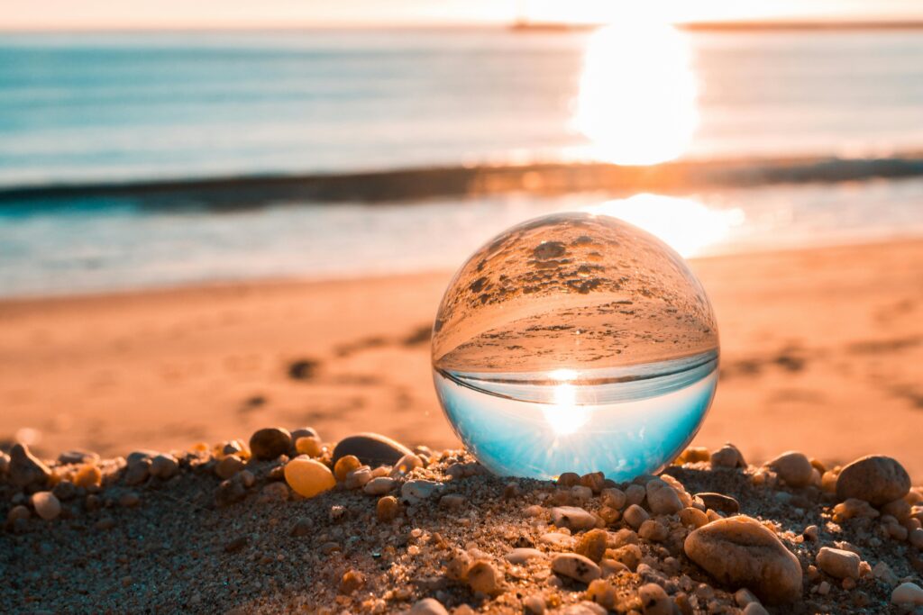 A tranquil beach scene with a lensball reflecting the sunrise over the ocean.